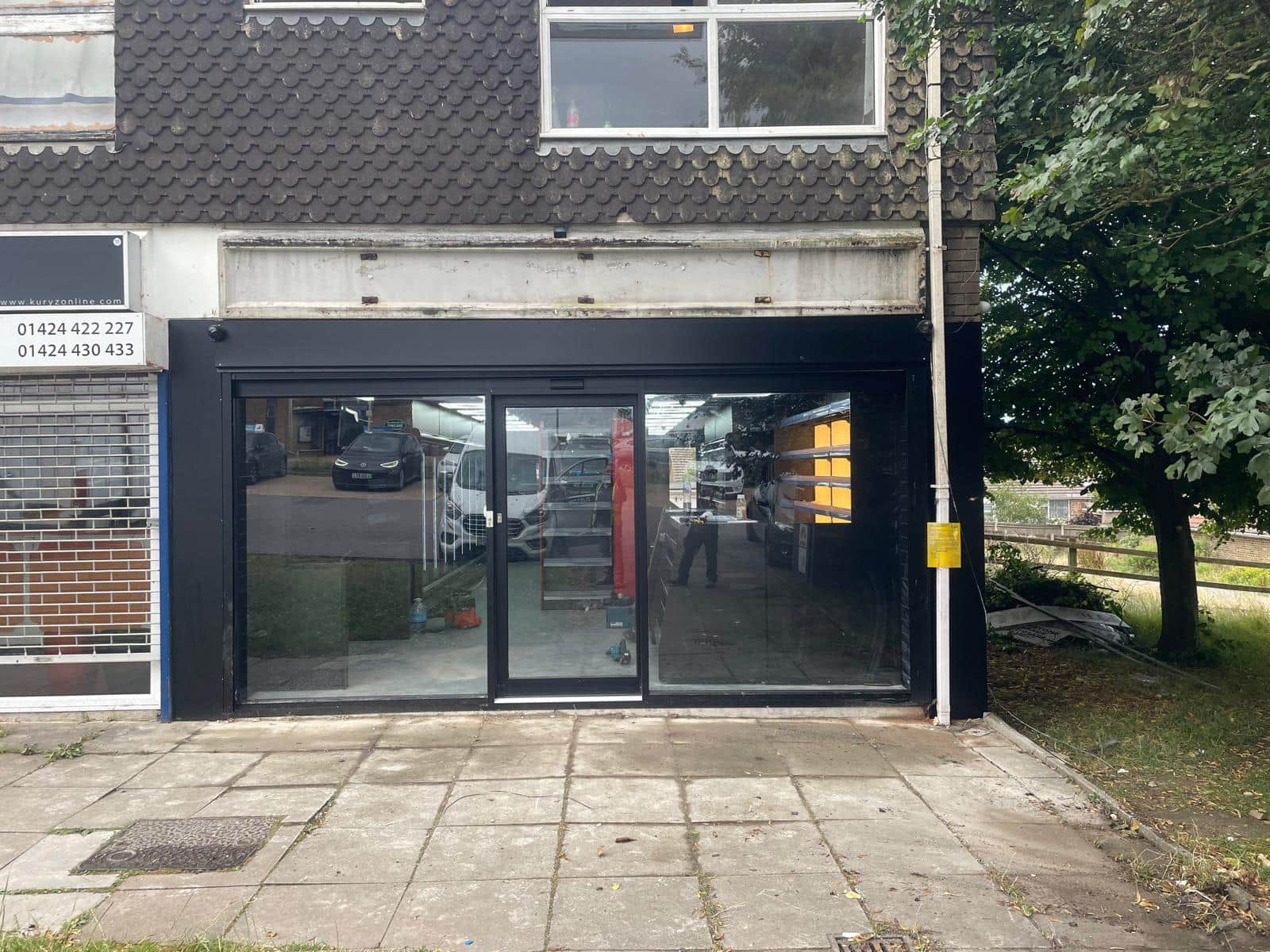 Single-storey retail unit with a new dark aluminium front and a pair of sliding glazed doors, between existing neighbouring units.