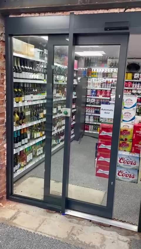 Automatic sliding door in a dark aluminium frame at a convenience store entrance.