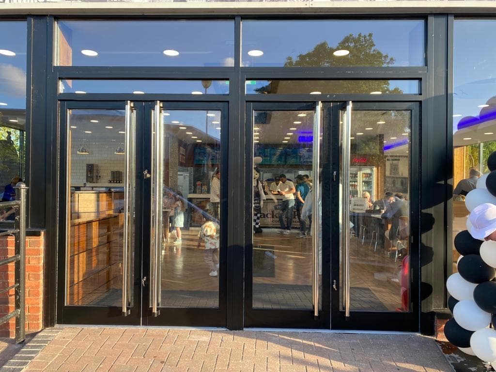 Pair of fully glazed aluminium entrance doors with long pull handles under a glazed fanlight